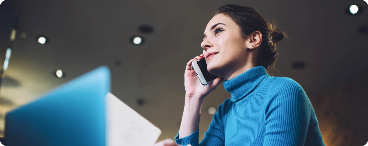 A professional woman in a blue sweater talking on the phone, symbolizing expert insurance business support.
